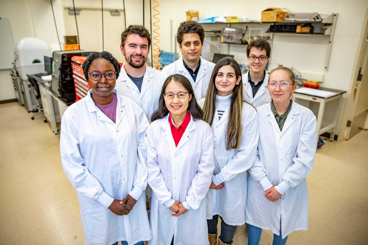 Group of researchers in crisp white lab coats stand together in a bright laboratory filled with equipment and workstations.